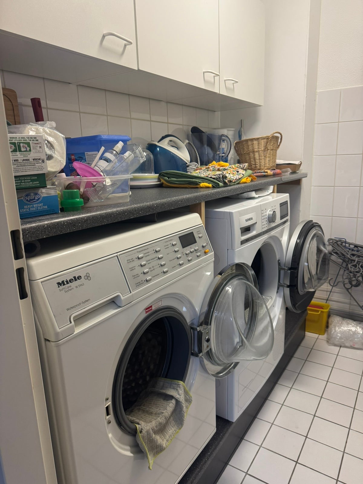 De oude wasruimte met losse wasmachine en droger onder een vol werkblad